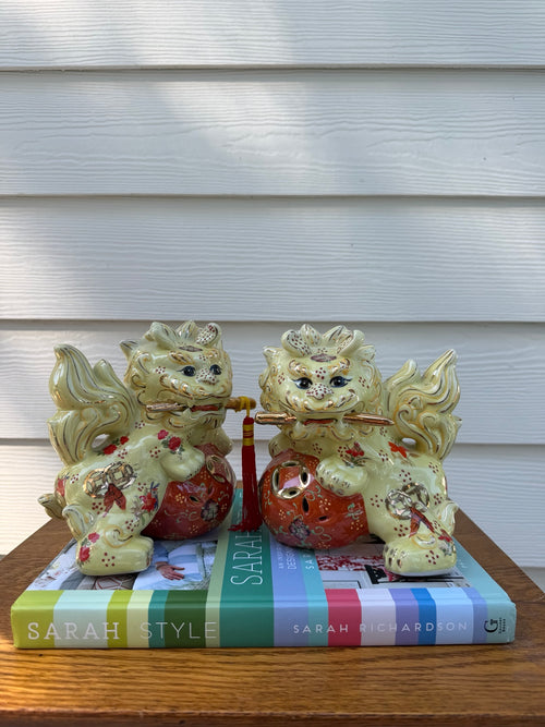 Pair of pale yellow ceramic foo dogs with coral floral balls and gold-tone details