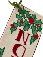 Portrait close-up of holly needlepoint, NOEL lettering and green ribbon bow
