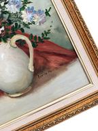 Close-up of floral still life showing the Lucille Merrill signature, canvas texture, cream liner, and ornate gold frame