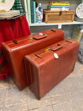 Larger vintage cognac-brown suitcase at the back and smaller suitcase in front, sold separately
