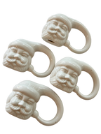 Angled view of four white glazed ceramic Santa napkin rings