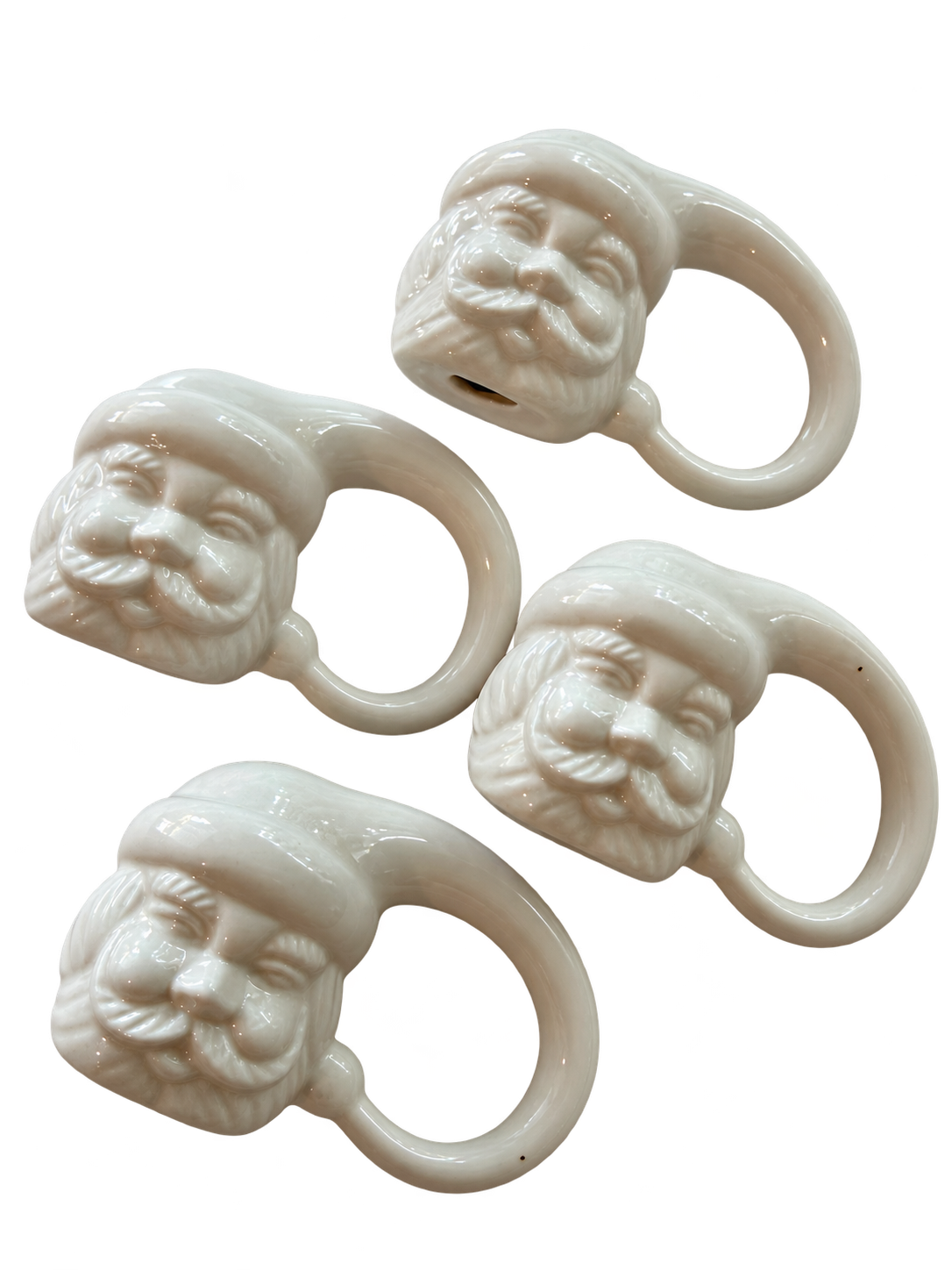 Angled view of four white glazed ceramic Santa napkin rings